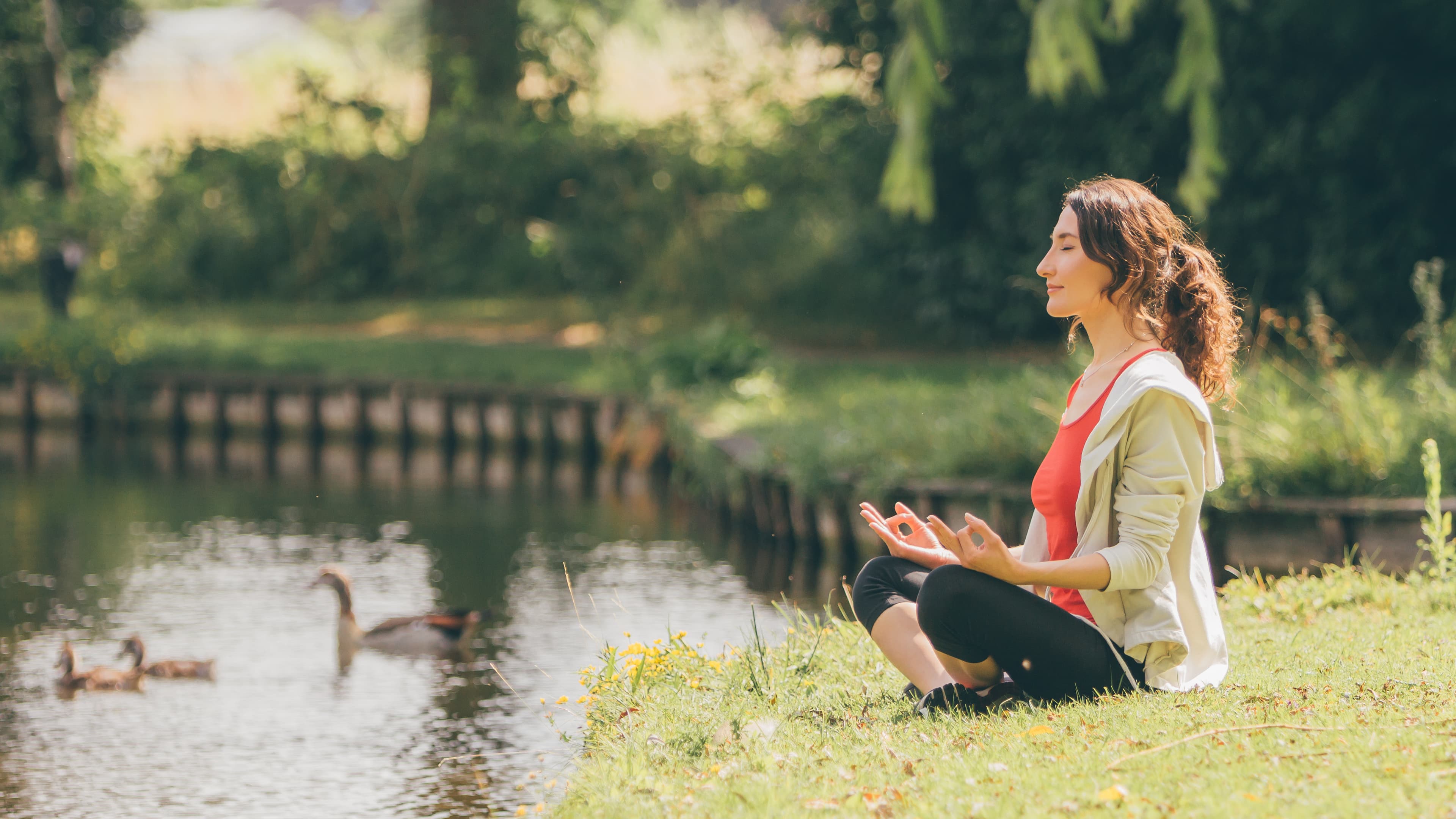 A woman meditating cross-legged beside a pond