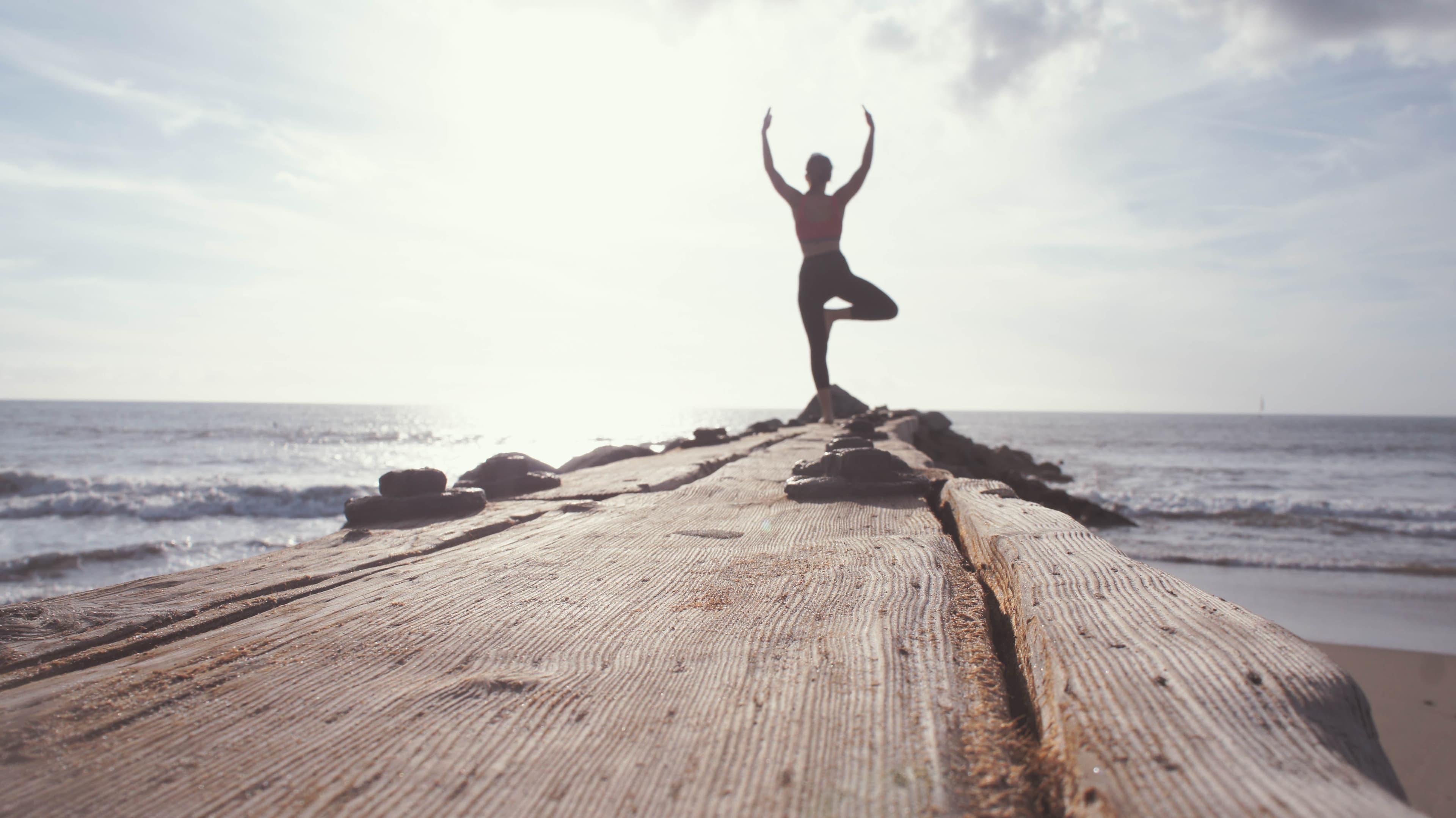A woman holding a yoga pose on the shoreline at sunset