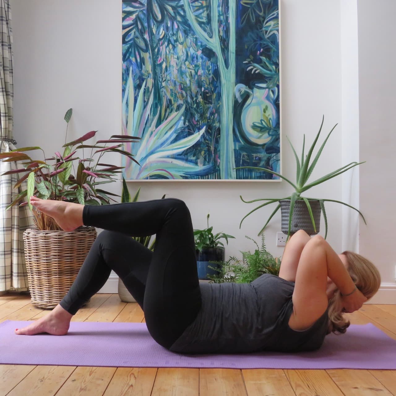 A woman lying on a mat performing a gentle somatic movement, lifting her head and shoulders